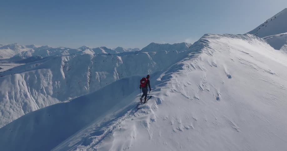 Skier holds his poles as he climbs up to the peak of a snow covered mountain