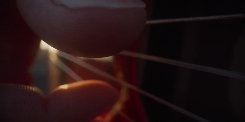 A close view of a man plucking the strings of an acoustic guitar as warm golden sunlight glints off the wood and creates a bright lens flare