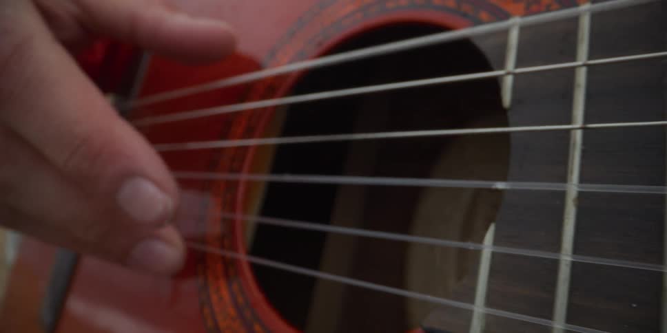 A person holding a red guitar and using their fingers to slowly strike the strings
