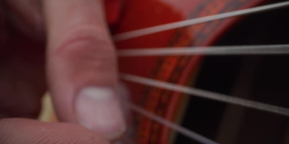 A person strumming the strings of a guitar with their fingers outdoors
