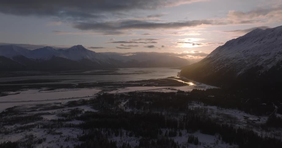 A landscape view of the horizon with a lake and a snowcovered mountain range as the sun rises