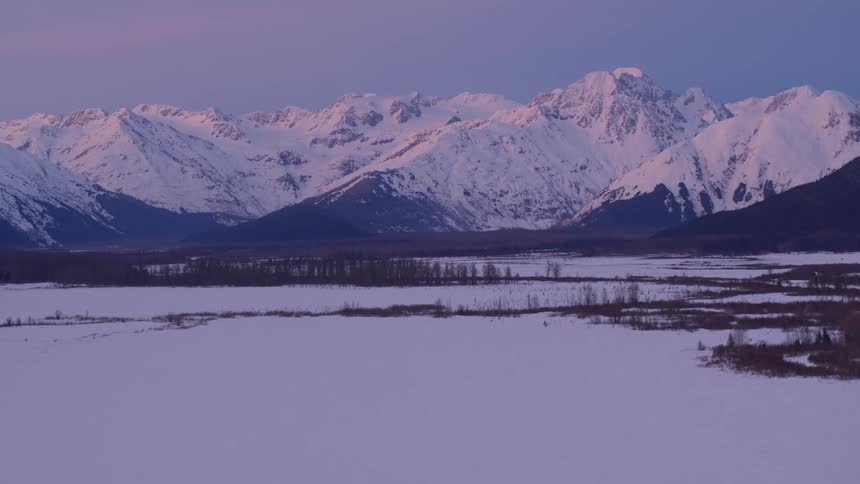 An aerial view of a landscape with mountains covered in the snow in the distance