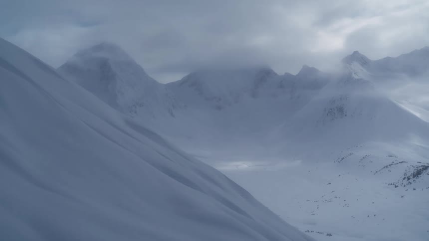 An aerial view shows snow covered mountain peaks and ridges under a cloudy sky