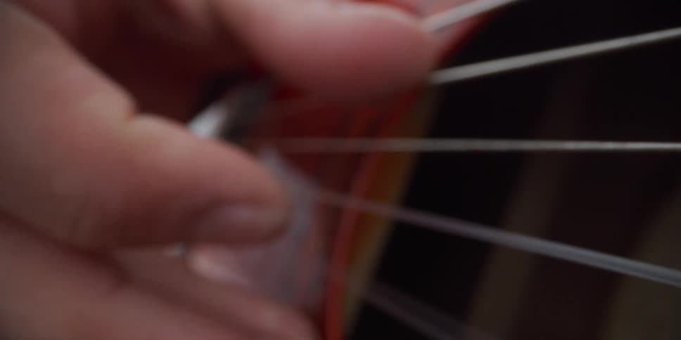 A person outdoors playing a red guitar hitting the strings with their fingers at midday