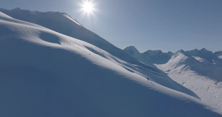 A person hiking up a snowy mountain in the arctic as the sun lights up the sky