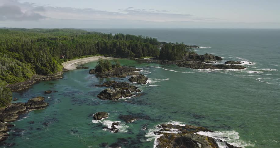 An expansive aerial shot slowly pulls back to reveal a beautiful and remote coastline with a hidden beach, dense forest, and rocky isles