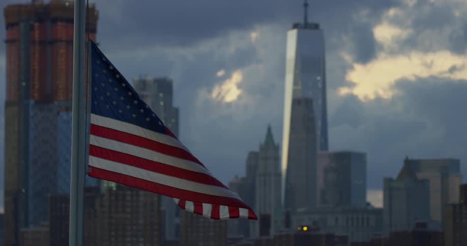 An american flag billows in the wind with skyscrapers in the distance