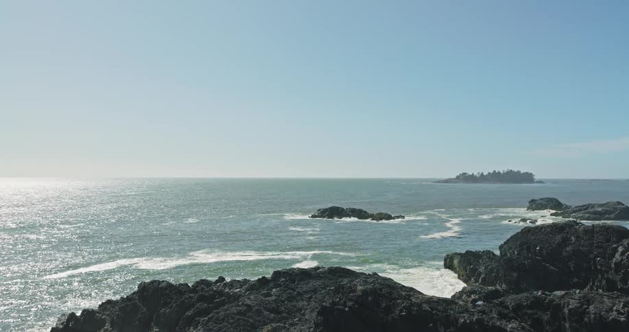 A stunning aerial view rises over a rugged, rocky coast to reveal the vast, sunlit Pacific Ocean on a clear day