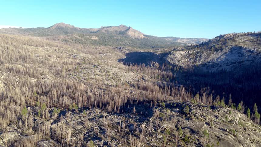 A slow aerial pullback reveals the devastating aftermath of a wildfire across a rocky, mountainous landscape