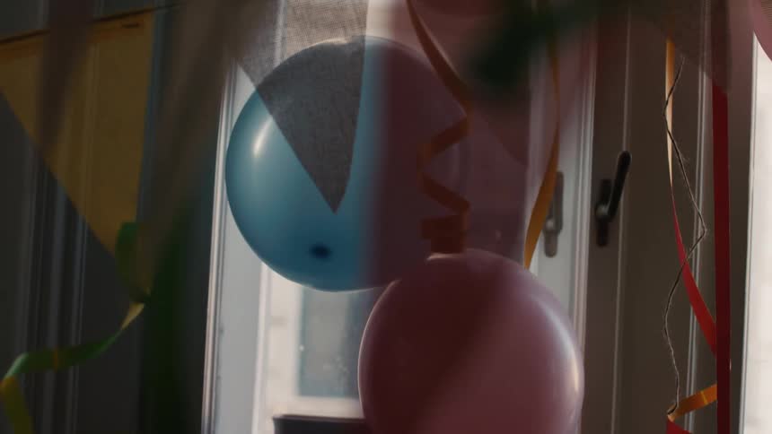 Colorful party balloons and streamers hang in a sunlit room, gently swaying after a celebration