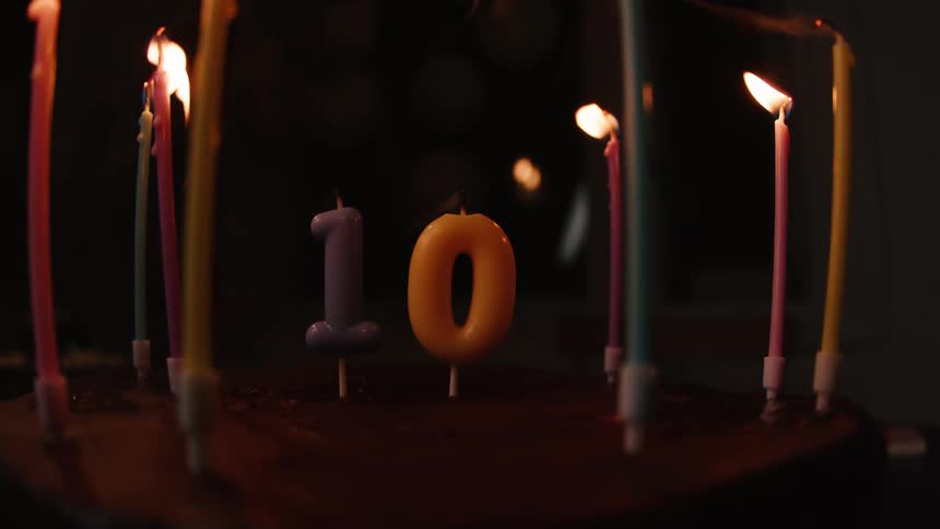 A close-up shot of candles on a tenth birthday cake being blown out in a dark room