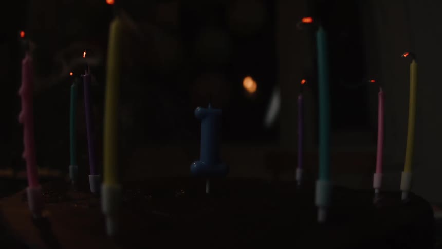 A close-up, slow-motion shot of candles on a first birthday cake being blown out in a dark room