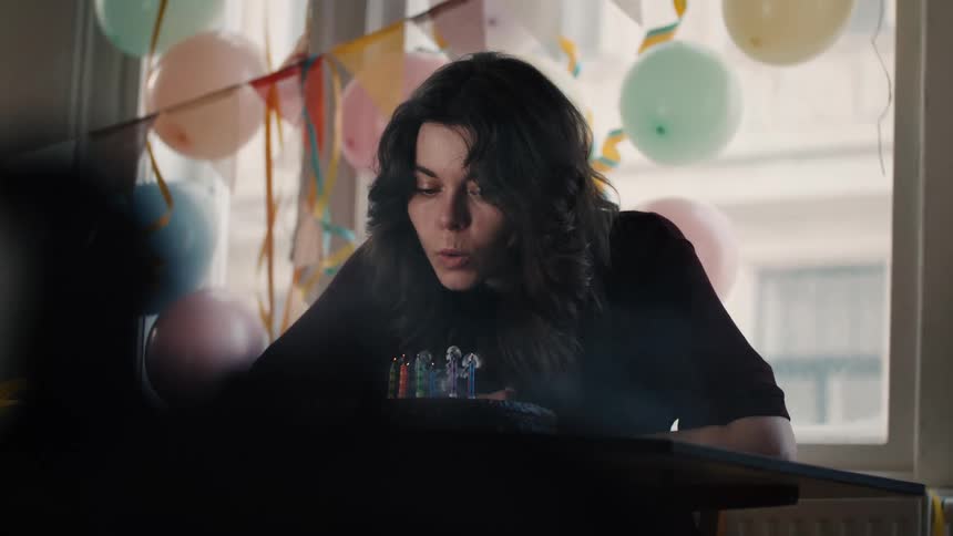 A pensive young woman celebrates her birthday alone, blowing out the candles on her cake in slow motion