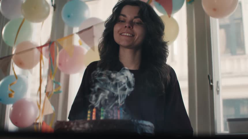 A happy woman smiles and makes a wish before blowing out the candles on her birthday cake in slow motion