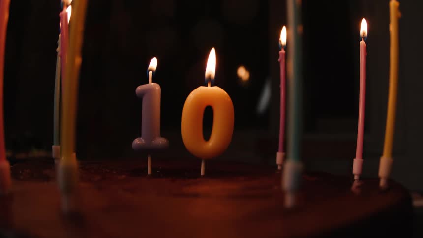 A hand with a lighter illuminates the number 10 candles on a chocolate birthday cake in the dark