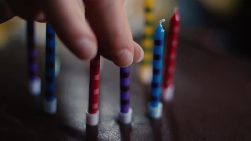 A hand carefully places a colorful striped candle into a rich chocolate birthday cake in slow motion