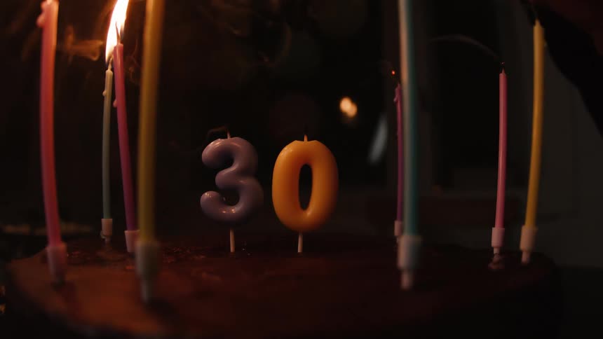 Colorful candles on a chocolate cake for a 30th birthday are blown out in slow motion