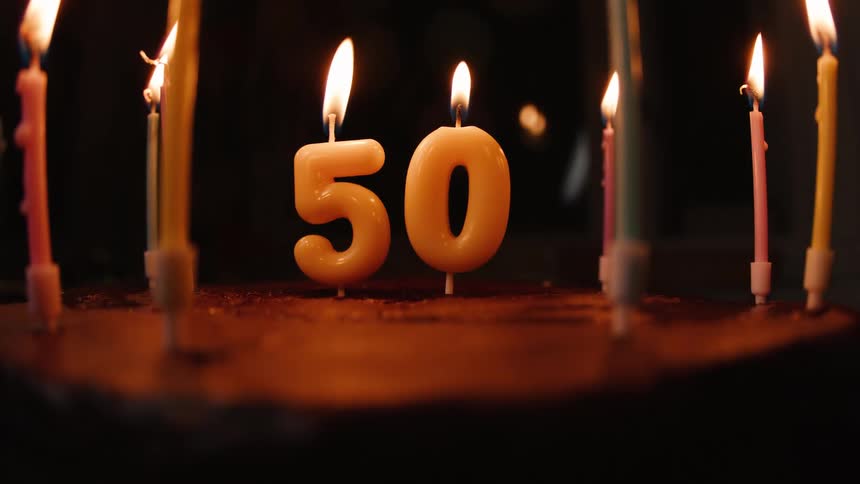 A person's hand uses a lighter to light the number 50 candles on a cake for a 50th birthday celebration