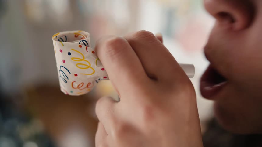 A festive party blower unfurls and retracts in a slow-motion close-up as someone blows into it