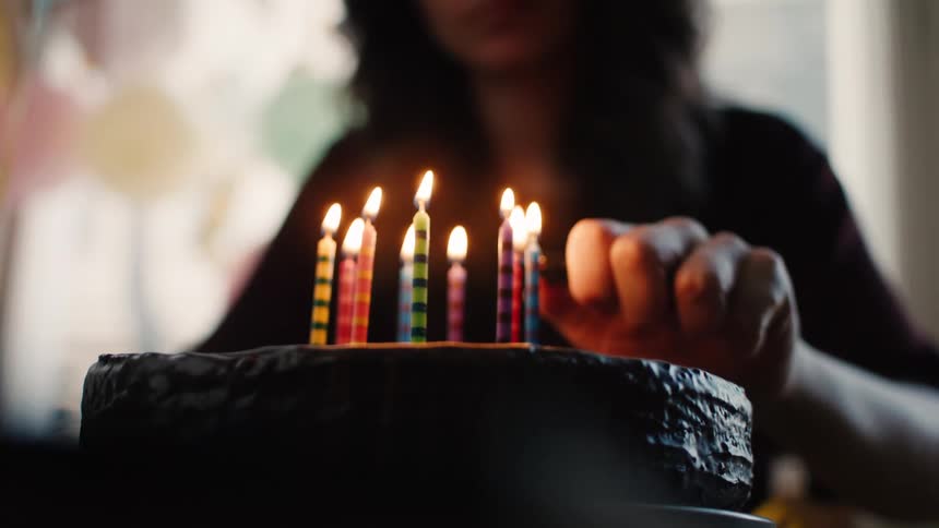A woman's hand carefully lights colorful striped candles on a rich chocolate birthday cake in slow motion