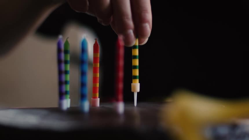 A close-up, slow-motion shot of a hand carefully placing a colorful striped birthday candle onto a chocolate cake