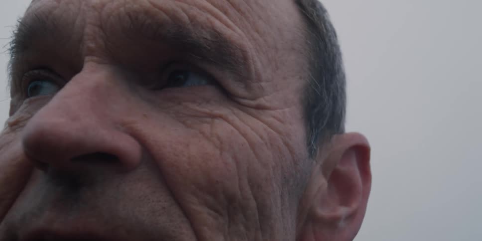 An extreme close-up of an elderly man's weathered face as he looks around thoughtfully on an overcast day