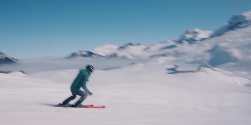 Dynamic follow shot of a skier carving down a sun-drenched mountain slope above a sea of clouds