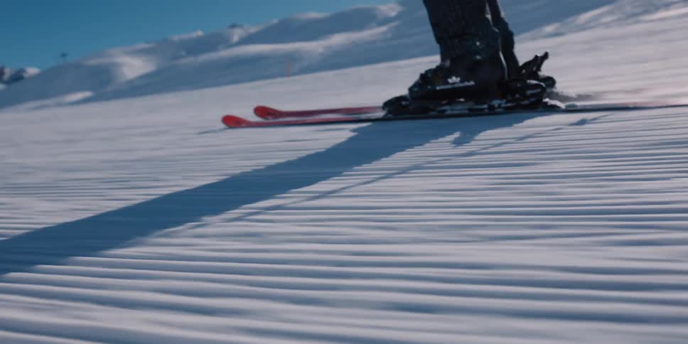A slow-motion close-up of a skier's legs gliding smoothly over freshly groomed snow on a sunny day in the mountains