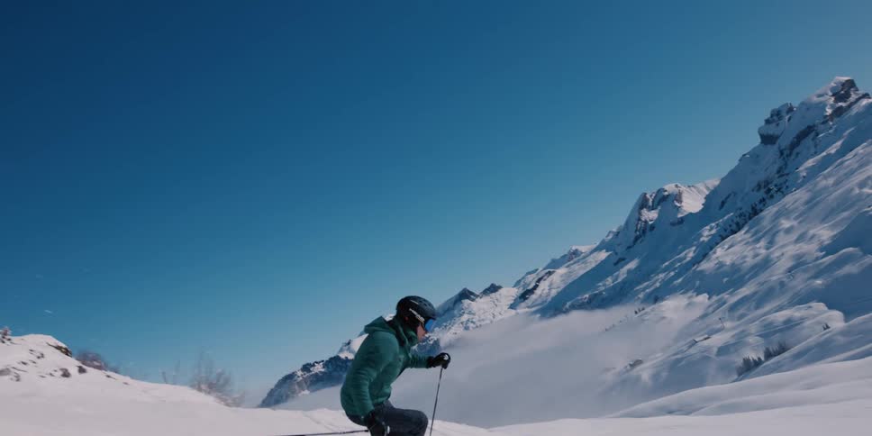 A skier gracefully carves down a pristine, snowy mountain slope on a beautiful sunny day in slow motion