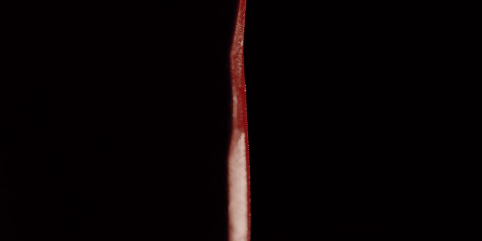 An extreme close-up reveals the textured surface and sharp edge of a red pointed object against a black background
