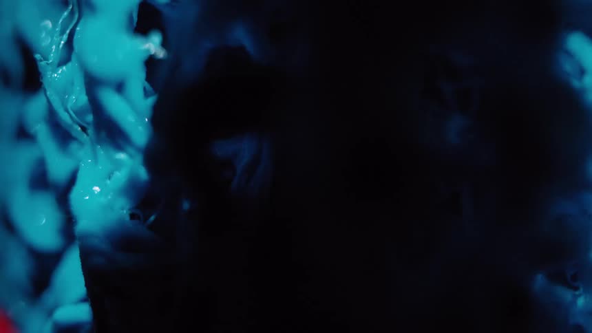 Abstract macro shot of a mysterious glowing blue substance shifting as ethereal smoke drifts across a dark background
