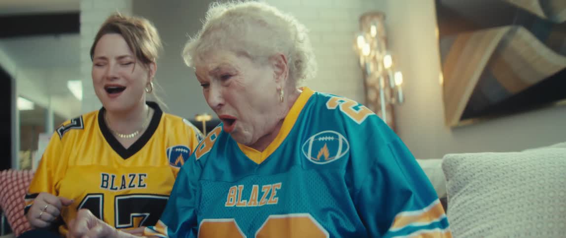 A young woman and her elderly mother dressed in football jerseys are heartbroken as they watch their team lose a game on a tablet in super slow motion