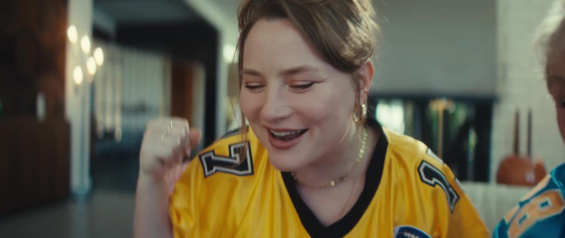 A grandmother and granddaughter in football jerseys cheer and celebrate excitedly while watching a game at home in slow motion