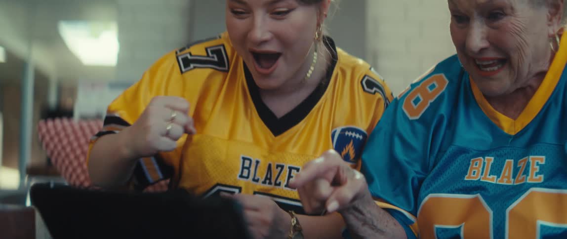 A slow-motion rack focus reveals two excited women in football jerseys cheering as they watch a game on a tablet