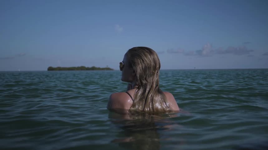 Woman in sunglasses stands shoulder deep in the water