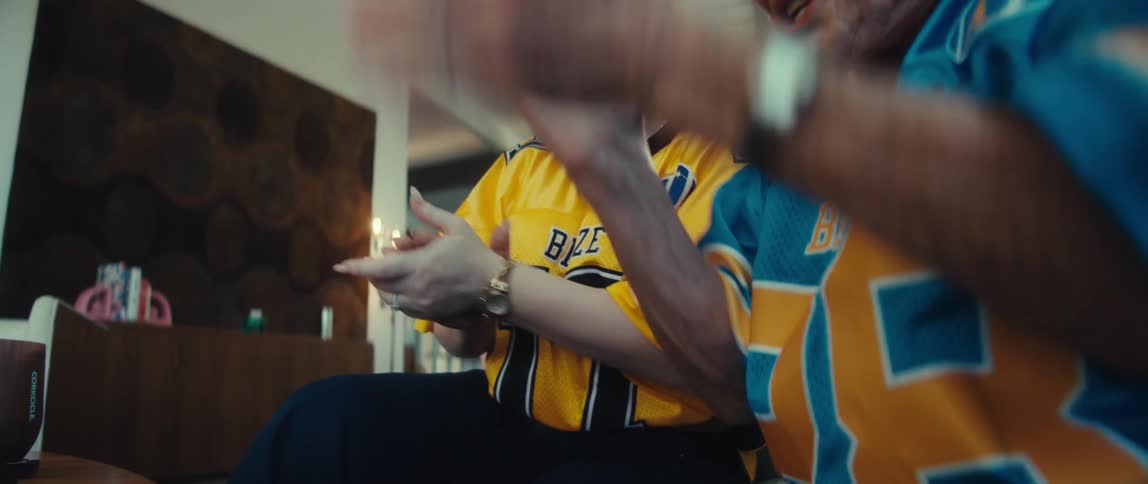 A close-up slow-motion shot of an elderly woman and a younger woman clapping with joy while watching a sports game in their jerseys