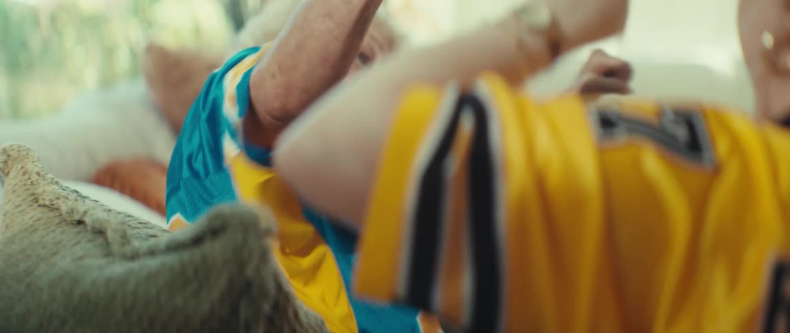 An elderly woman wearing a 'Legend' jersey and a younger person in a 'Rookie' jersey celebrate a victory with an excited fist bump while watching a game together