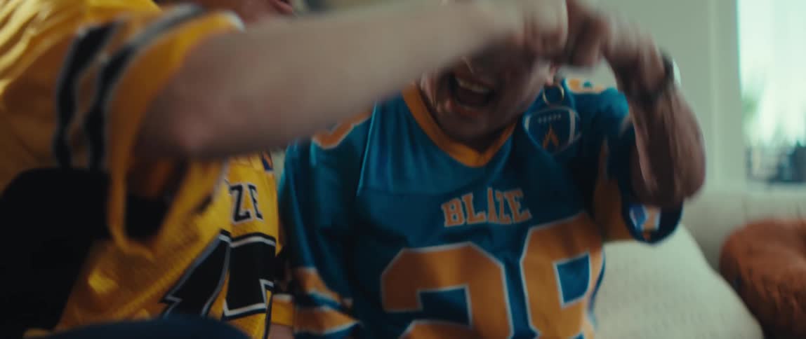 A senior woman and a younger woman wearing football jerseys celebrate ecstatically in slow motion while watching a game on a tablet