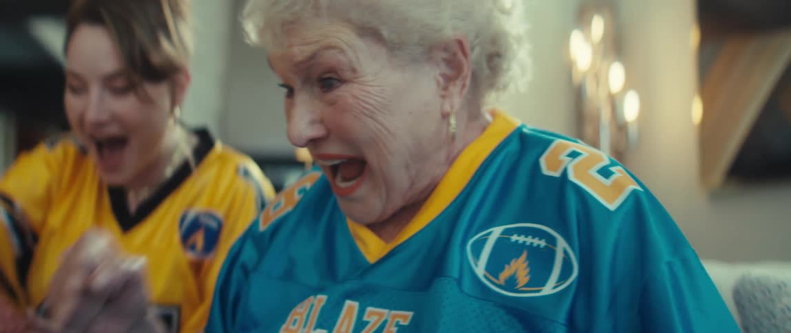 A passionate elderly football fan in a jersey cheers and celebrates in slow motion while watching a game at home