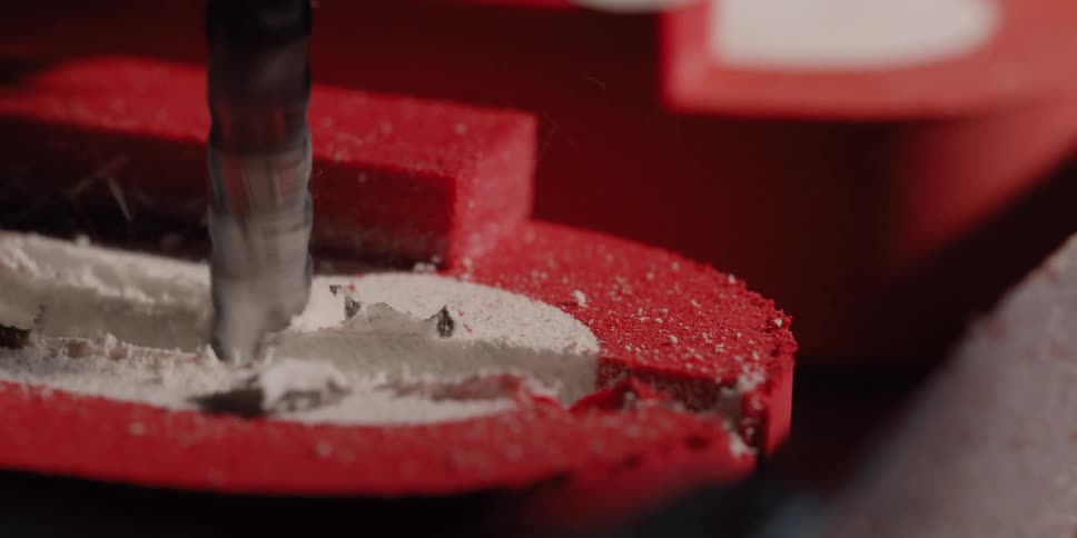 A CNC router bit carves a path through a red material in extreme slow motion, revealing the white core underneath
