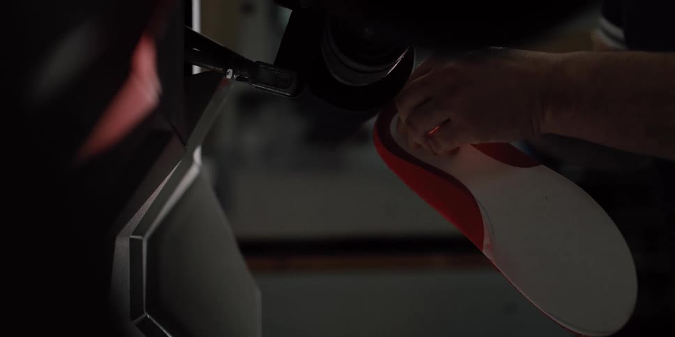 A skilled worker carefully shapes a custom orthopedic insole by sanding its edges on a machine in a workshop