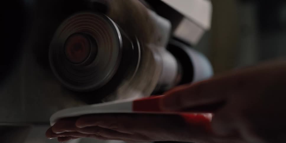 A focused craftsman carefully sands the edge of a shoe sole on a spinning industrial finishing machine in a dimly lit workshop