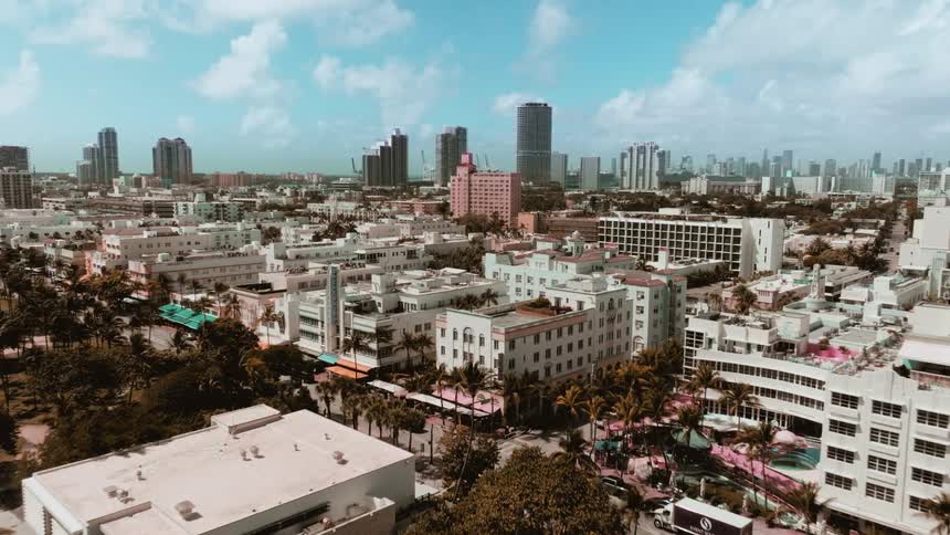 A slow aerial push-in shot over the Art Deco hotels and palm trees of Miami's South Beach on a sunny day