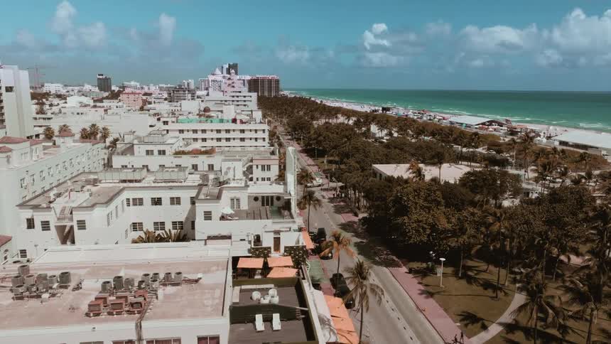 Stunning aerial view flying over the buildings of Miami's South Beach, revealing the famous Ocean Drive and the beautiful coastline on a sunny day