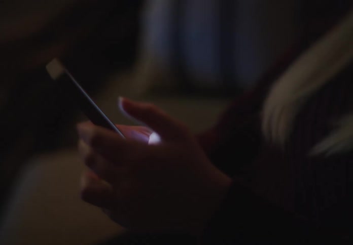 Close-up of a woman's hands scrolling and typing on a smartphone screen in a dark room