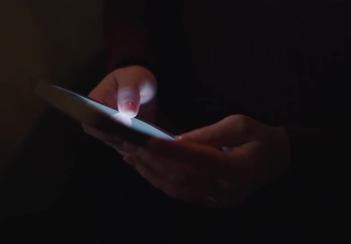 Close-up shot of hands scrolling and typing on a smartphone screen in a completely dark room