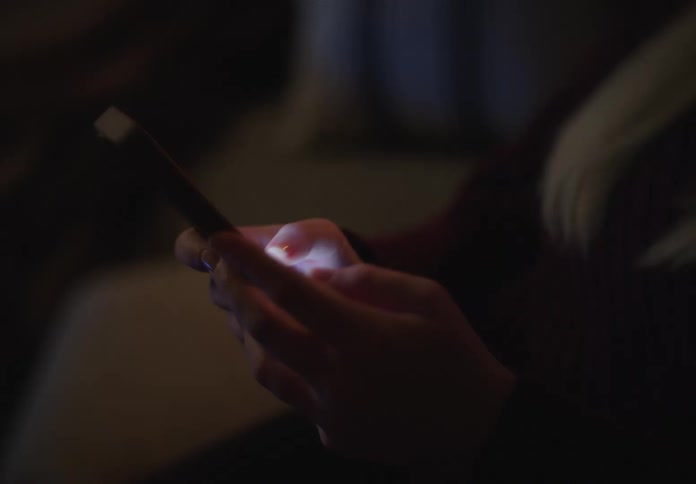Close-up on a person's hands as they scroll through their smartphone in the dark of night