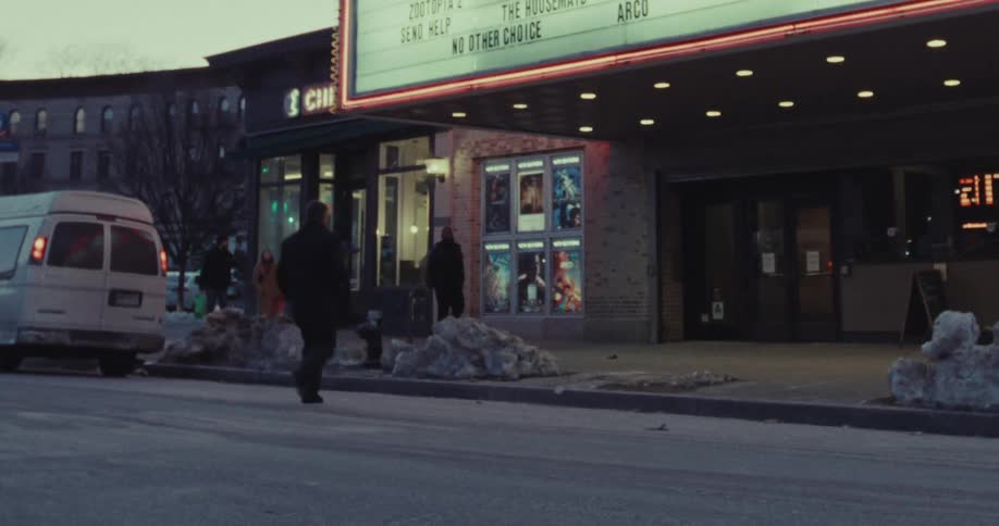 A man crosses the street in front of a movie theater on a cold winter evening in the city