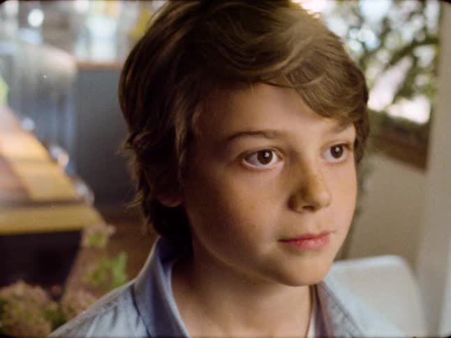 Close-up of a thoughtful young boy with brown hair and freckles looking up with a gentle smile, shot with a vintage film look