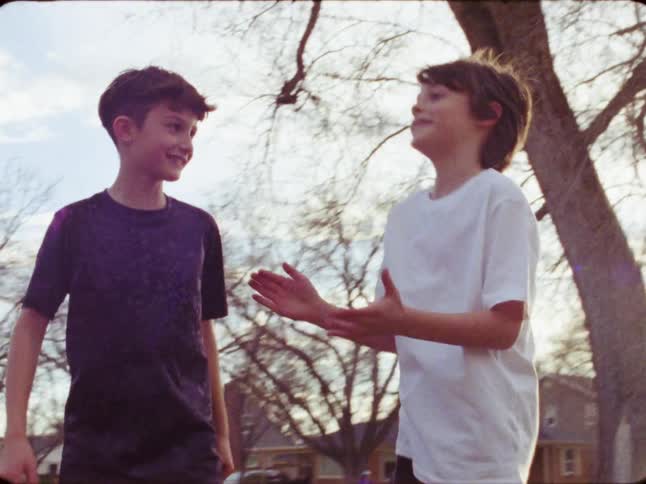 Authentic 8mm vintage-style footage shows two young boys happily playing together in a suburban park on a sunny day